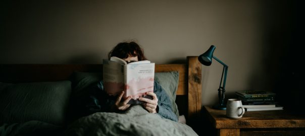 A person reading in bed beside a desk lamp