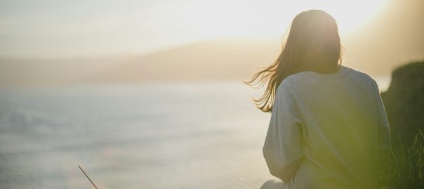 A woman sitting by the sea in soft evening light